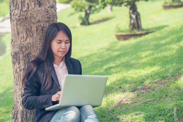 Asian woman sitting green park using laptop computer. 
