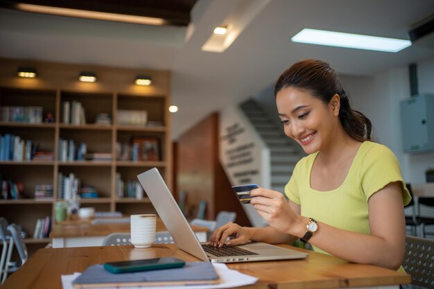 Foto donna asiatica seduta e con in mano una carta di credito per fare acquisti online con il portatile e lo smartphone a casa