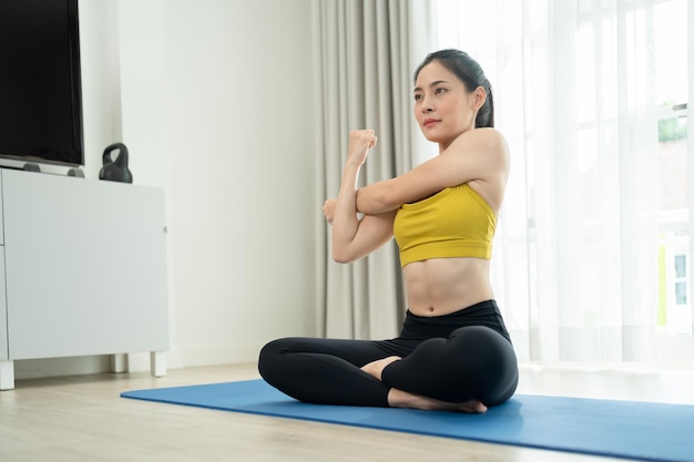 Donna asiatica seduta sulla stuoia che allunga le mani che esercitano yoga in soggiorno a casa