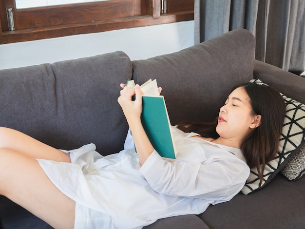 Asian woman sitting and read book on sofa at home 