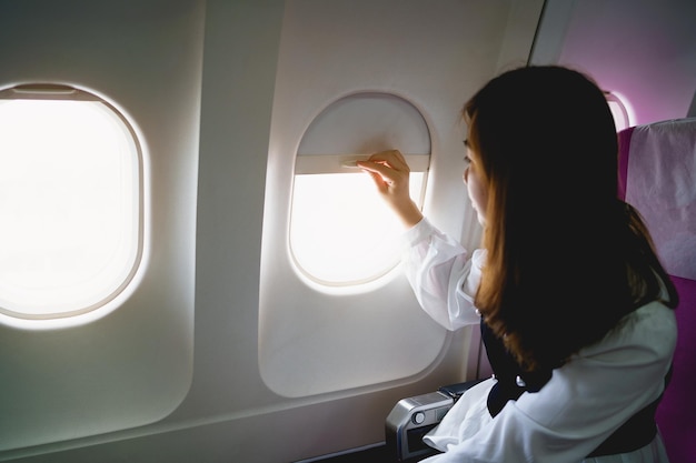 Asian woman sitting in a seat in airplane and looking out the\
window going on a trip asian woman passenger is leaving for a trip\
by plane on vacation vacation travel concept