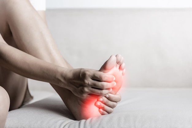 Asian woman sitting on sofa feeling pain in her foot at home