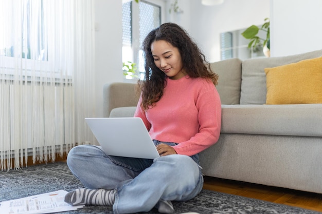 Donna asiatica seduta con il computer sul divano che studia a casa elearning e concetto di lavoro freelance remoto