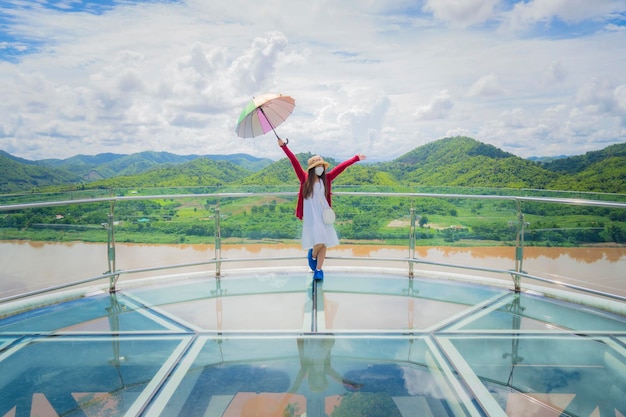 Skywalk 유리 다리에 있는 아시아 여성은 Phu Khok Ngio Chiang Khan Loei Thailand에서 태국과 라오스 사이의 새로운 랜드마크 관점입니다.