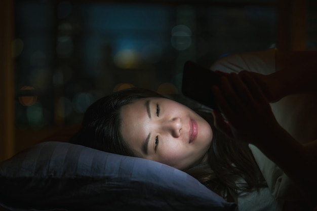 Donna asiatica che dorme e usa uno smartphone per social network o videoconferenze