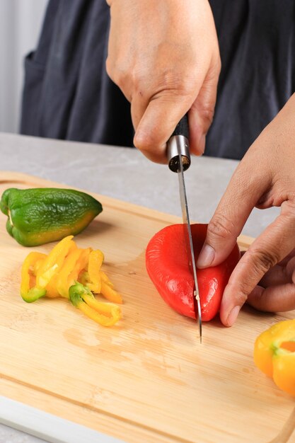 Asian Woman Slicing Yellow Red and Green Bell Pepper above Bamboo Cutting Board