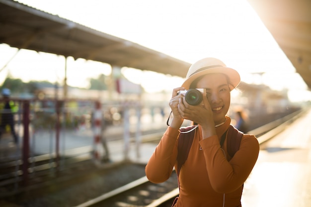 アジアの女性はカメラで笑顔し、駅で写真を撮る。