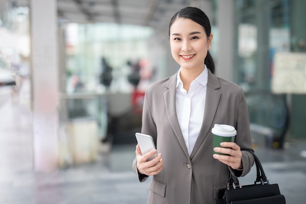 Asian woman smile with smartphone standing against street blurred building background