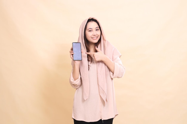 Asian woman smiles cheerfully at the camera holding her hand and pointing at her cellphone gadget sc