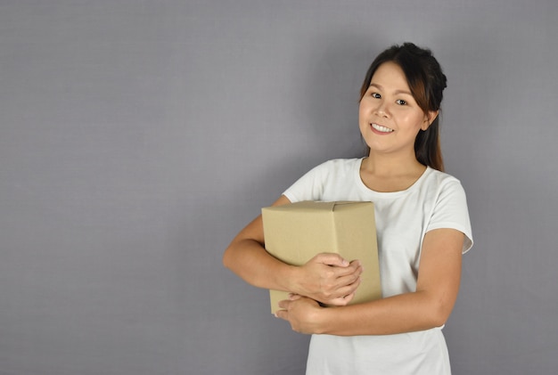 Asian woman smiling holding package box on grey . 