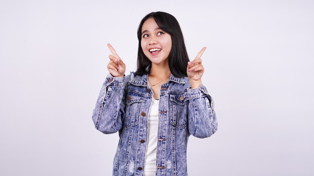 Asian woman smiling wearing jeans jacket and  pointing finger hands up with isolated white surface