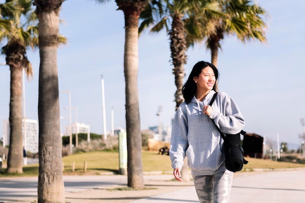 Asian woman smiling while walking with yoga mat