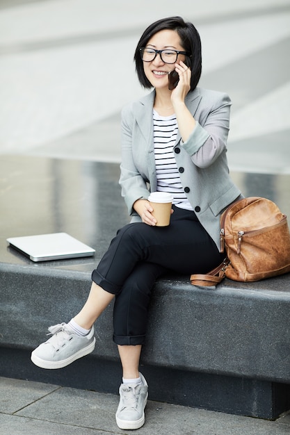 Asian Woman Speaking by Smartphone Outdoors