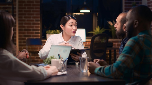 Asian woman speaking financial report in business meeting, employee discussing corporate presentation at table. Coworkers brainstorming, company marketing research analytics discussion