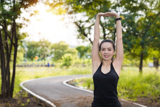 朝の公園で屋外でのトレーニングの前にストレッチをしているスポーツ衣装を着たアジアの女性