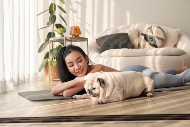 Asian woman in sportswear exercising and doing yoga with cute dog in living room at home