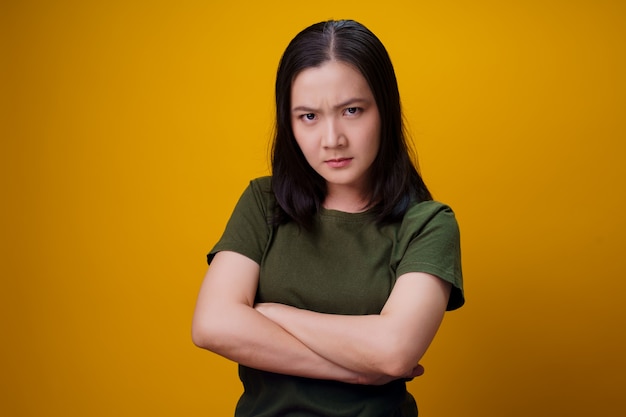 Азиатская женщина, стоящая и сердитая, изолирована над желтой стеной.