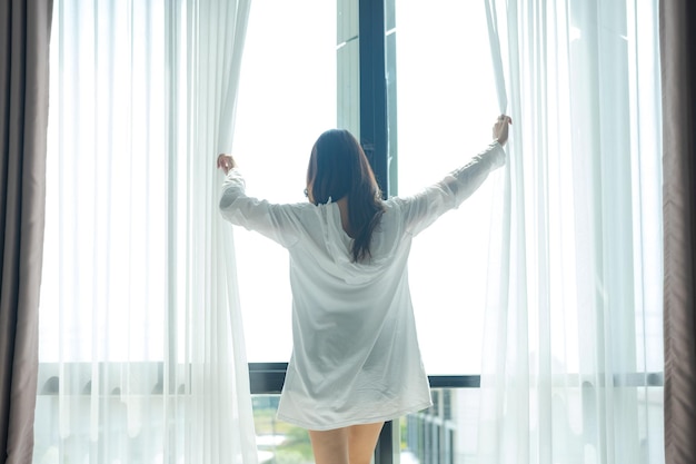 asian woman standing by the window and stretching in the morning