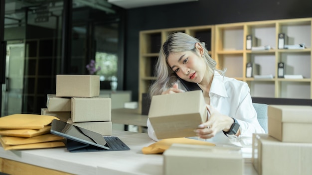 Asian woman startup small business entrepreneur freelance young\
success business asian woman online marketing packaging box and\
delivery check online orders to prepare pack the box selling\
product