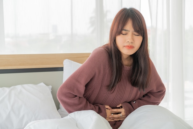 Asian woman stomachache and sleeping on bed