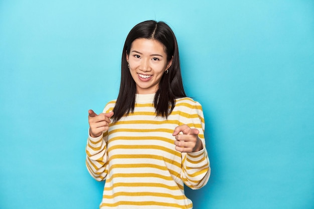 Asian woman in striped yellow sweater pointing to front with fingers
