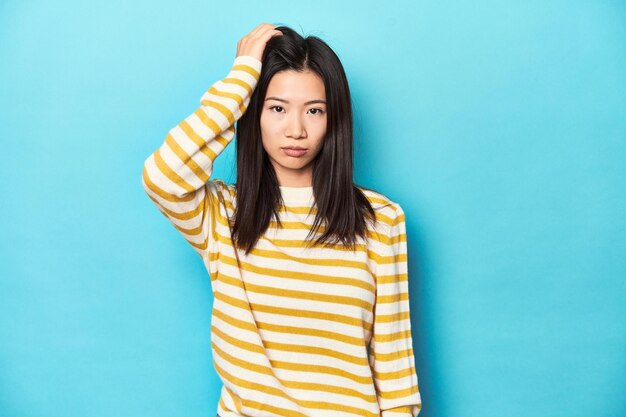 Asian woman in striped yellow sweater tired and very sleepy keeping hand on head