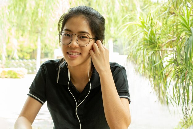 Asian woman student working on laptop with earphone looking at camera.