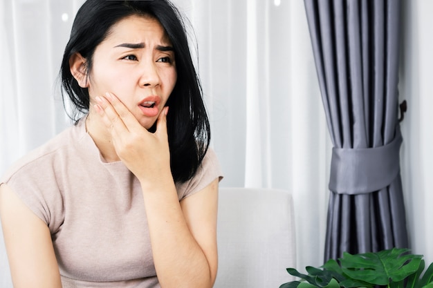 Donna asiatica che soffre di problemi di mal di denti mano che tiene una gengiva dolorosa al viso