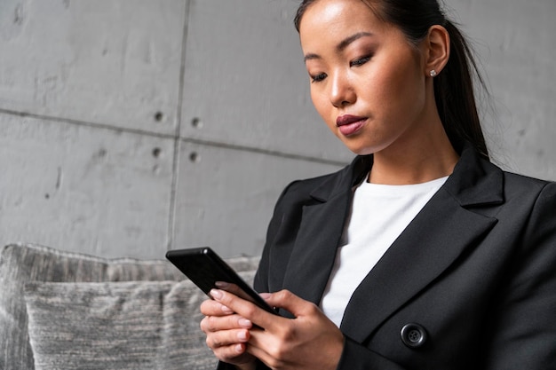 Asian woman in suit web surfing in armchair