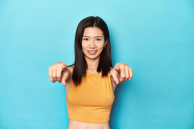 Asian woman in summer yellow top studio setup cheerful smiles pointing to front