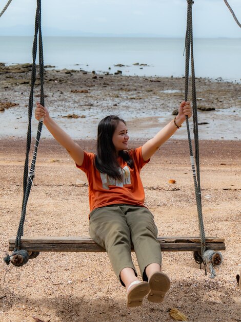 タイ南部の休日にビーチでブランコに揺れるアジア人女性。