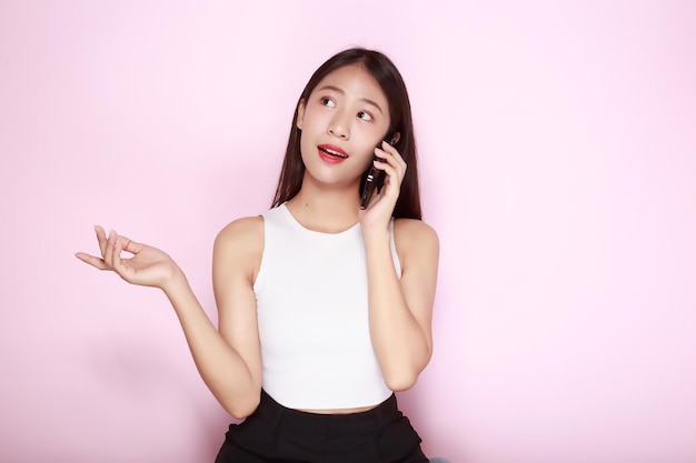 電話で話しているアジア人女性明るいピンクの背景の美しい若い女性の肖像画スタンドポジションで幸せで笑顔の投稿