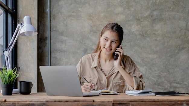 Asian woman talking on the phone she is a salesperson in a startup company she is calling customers to sell products and promotions Concept of selling products through telephone channels