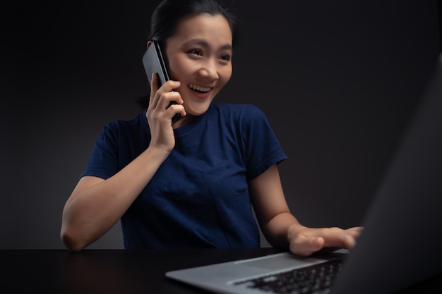 Asian woman talking on smartphone and working with laptop.