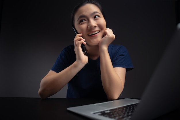 Asian woman talking on smartphone and working with laptop.