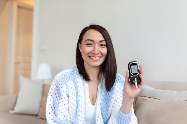 Asian Woman testing for high blood sugar Woman holding device for measuring blood sugar Woman doing blood sugar test Woman checking blood sugar level by glucometer and test stripe at home