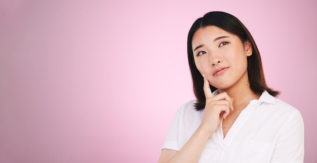 Asian woman thinking and decision on mockup in problem solving against a pink studio background Female person with idea solution or choice in memory reminder or brainstorming on mock up space