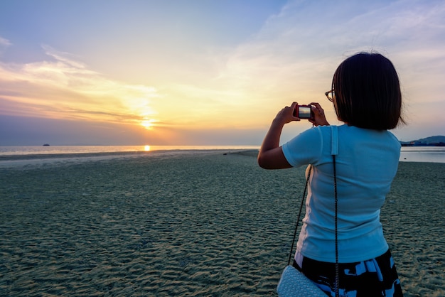 Foto turista asiatico che prende foto sulla spiaggia e sul bellissimo paesaggio naturale di cielo e mare colorati durante un tramonto al punto di vista del tramonto di nathon nell'isola di samui, surat thani, thailandia