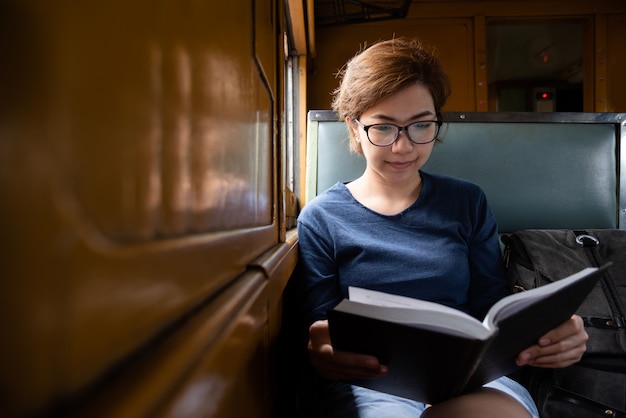Photo asian woman tourist wear glasses reading book inside train.