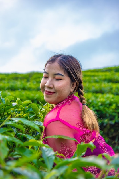 an Asian woman in a traditional pink costume is standing very elegantly in a tea plantation during the day