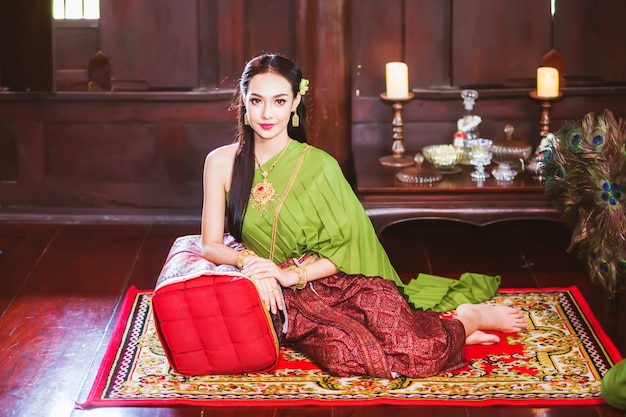 伝統的なタイのドレスを着て、タイ風の木造家屋に座っているアジアの女性。