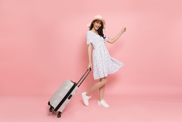 Asian woman traveler drag luggage isolated on pink background