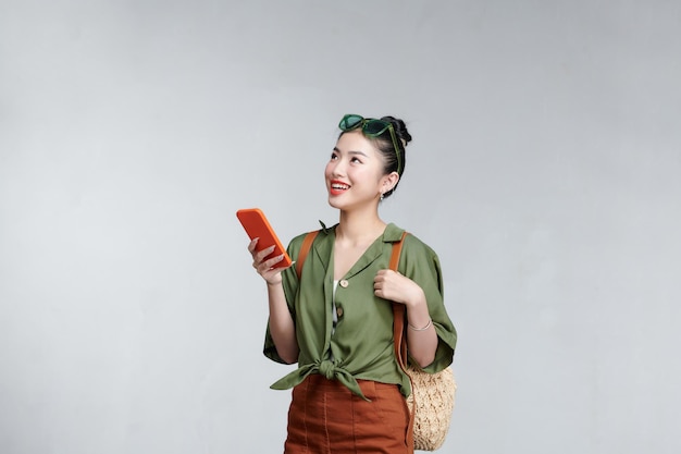 회색 배경 위에 휴대폰과 여름 여행 개념을 들고 있는 아시아 여성 여행자