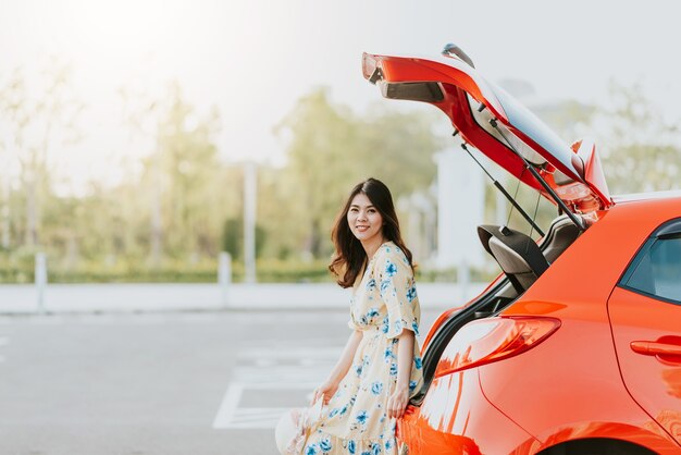 Азиатская женщина-путешественница, сидящая на багажнике автомобиля