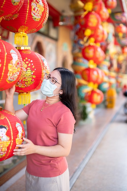Азиатская женщина-путешественница носит защитную маску с микробами и красным цветом с бумажными фонариками с китайским текстом «Благословения», написанным на нем, это украшение комплимента благословения удачи в китайском храме, китайский Новый год