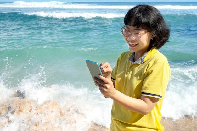 Asian woman traveling on the beach while using her mobile phone