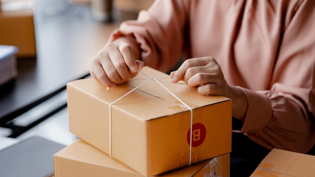 An Asian woman tying a parcel to a customer's box she owns an online store she packs and ships through a private transport company Online selling and online shopping concepts