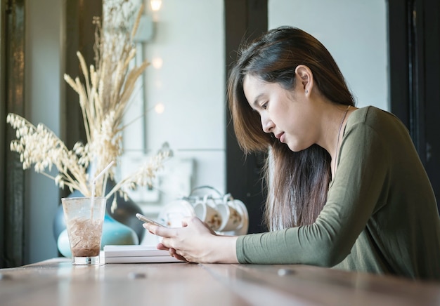 asian woman use a smartphone and drinking iced chocolate at the wooden counter desk in coffee shop