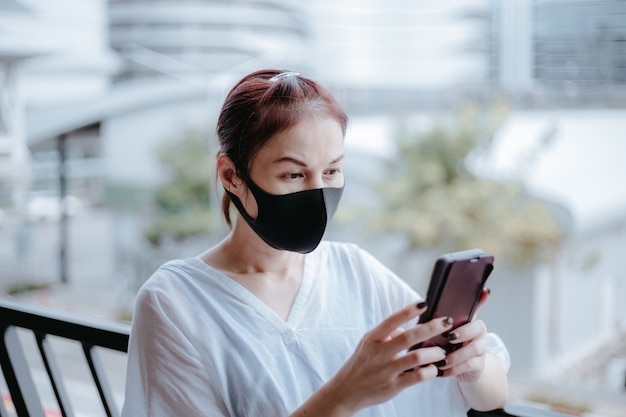 아시아 여자는 도시 거리에 의료 마스크 스마트 폰을 사용합니다.