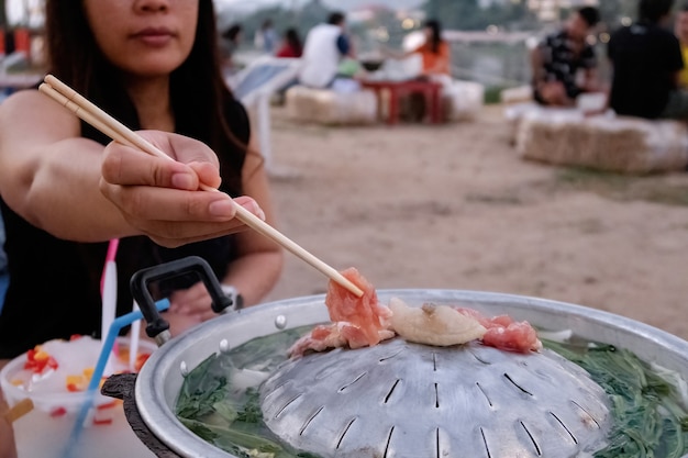 사진 젓가락을 사용하여 고기, 야채 및 국물을 구우는 아시아 여성은 돼지 고기 팬-moo kra ta라고합니다.